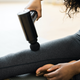 woman using a massage gun on her thigh